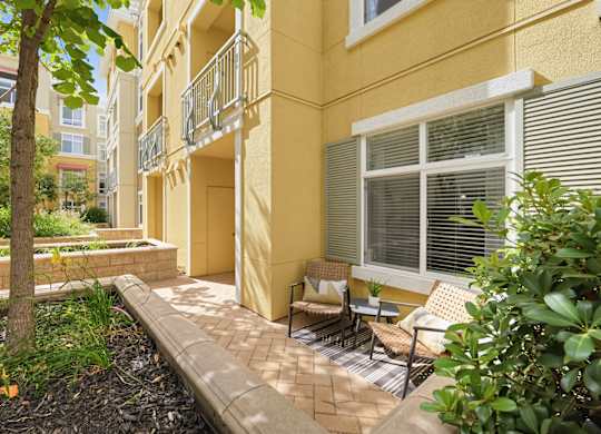 A yellow building with a balcony and a tree in front.