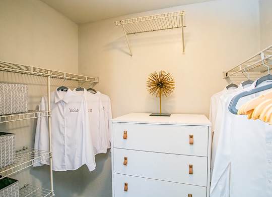 a closet with white clothes and a dresser and a rack of shirts