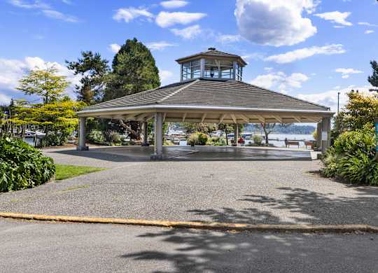 A gazebo with a tower is surrounded by greenery and a paved area.