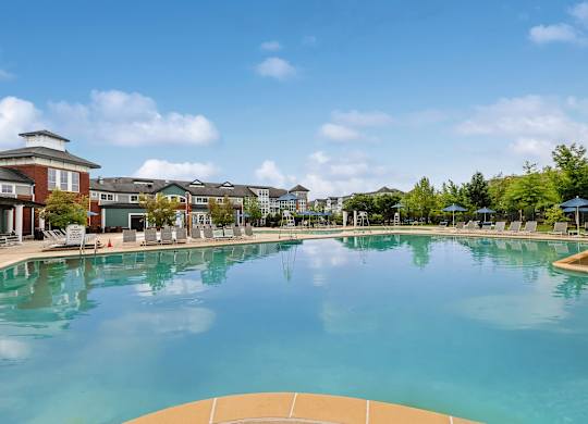 A large swimming pool in front of a building with a blue sky and clouds in the background.