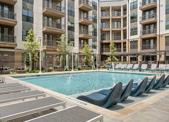 A pool area with lounge chairs and apartment buildings in the background.