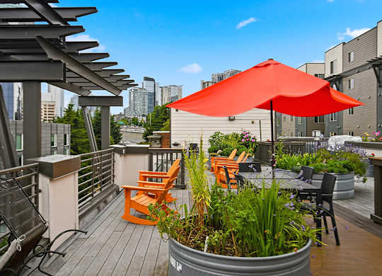 A red umbrella is on a wooden deck with a metal planter.