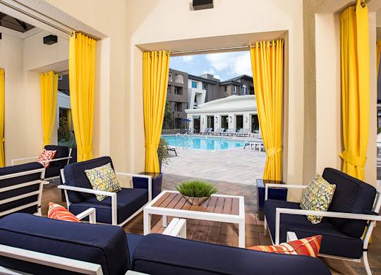 A patio with blue couches and yellow curtains overlooking a pool.