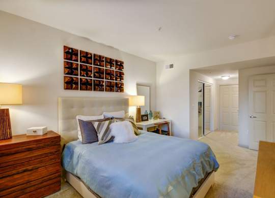 A bedroom with a bed, nightstand, and a wall hanging.