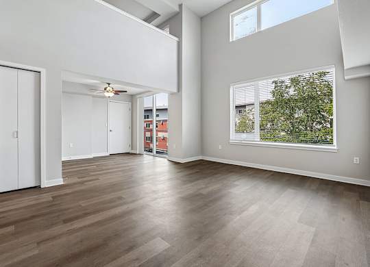 A large, empty room with wooden floors and a window overlooking a green outdoor area.
