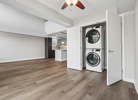 A washer and dryer are in a small closet in a large empty room.