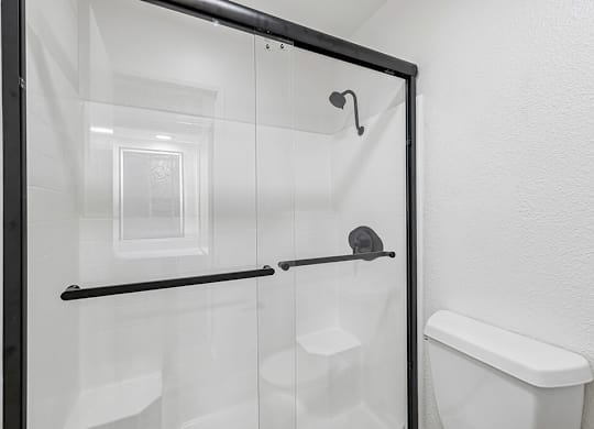 A white toilet is in a small bathroom with a glass shower door.