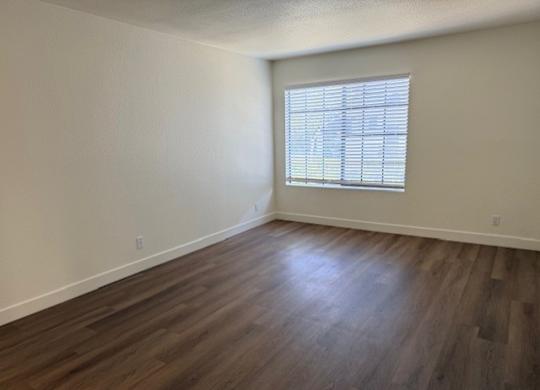 A room with wooden flooring and a window with blinds.