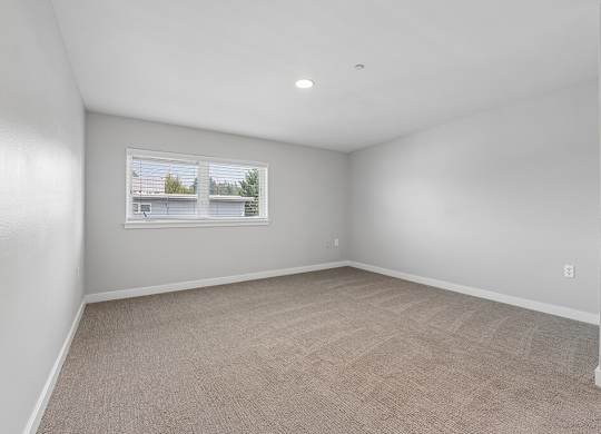A room with a carpeted floor and a window showing a view of a house.