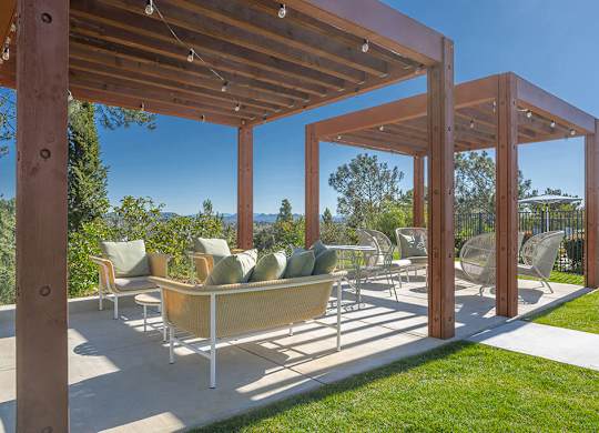 A wooden pergola with a couch and chairs under it.