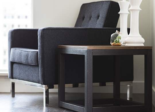A black chair and table with a white vase on it.