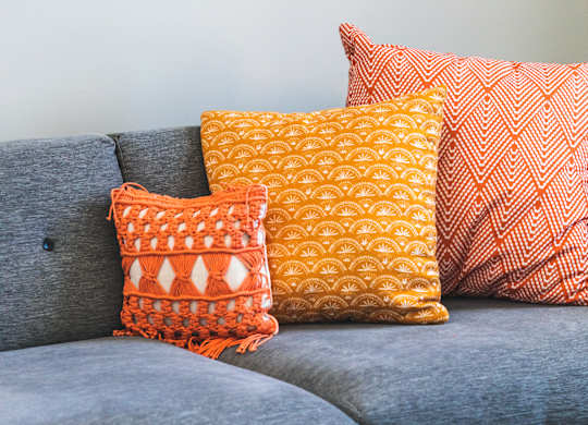 A grey couch with three pillows and a chess board on a table.