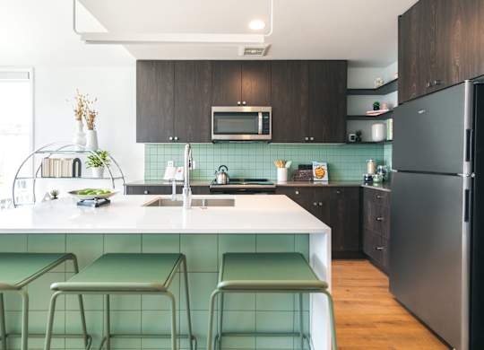 A kitchen with a black refrigerator and green bar stools.