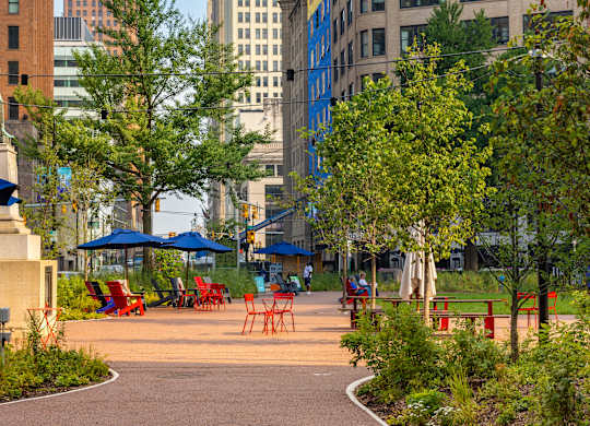 Capitol Park with a walking path and benches in the foreground and a city skyline in the background.
