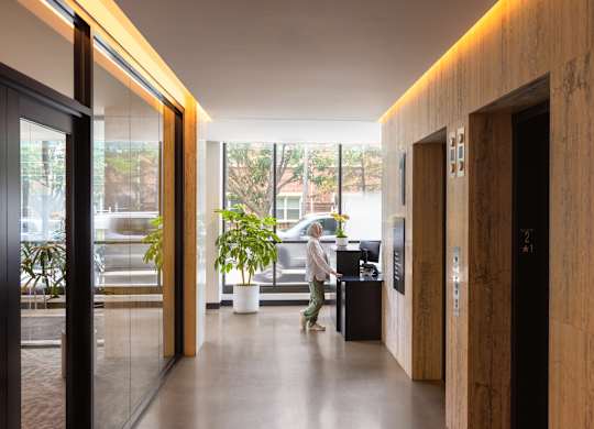 A woman is walking through a hallway with a plant on the left and a door on the right.