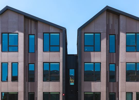 Two identical buildings with brown and beige facades and blue sky in the background.