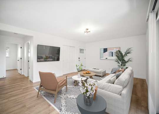 A living room with a grey couch, a brown chair, a coffee table with a vase of flowers, and a flat-screen TV mounted on the wall.