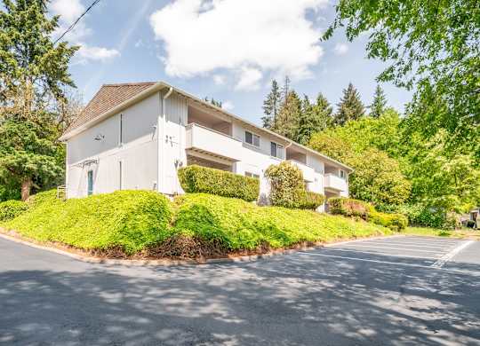 A white building with a brown roof is surrounded by greenery.