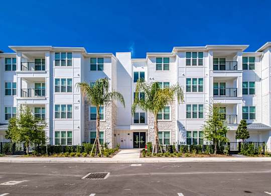 an apartment building with a parking lot and palm trees at Altis Twin Lakes Apartments, Kissimmee