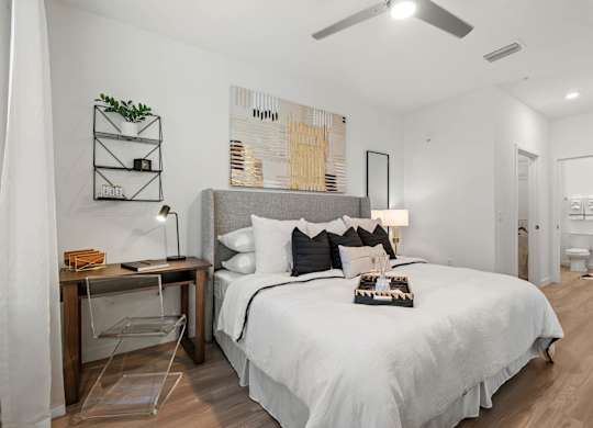 A bedroom with a bed, desk, chair, and a ceiling fan.