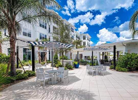 A patio area with tables and chairs and a striped umbrella.