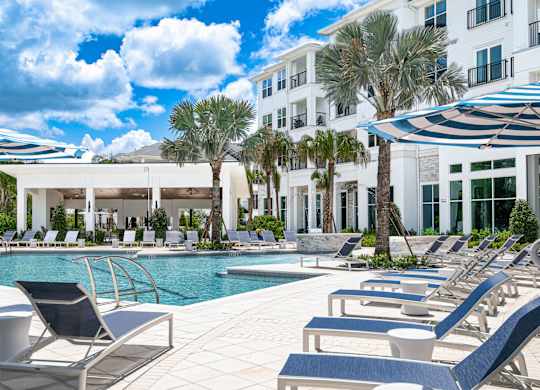 A pool area with sun loungers and a white building in the background.