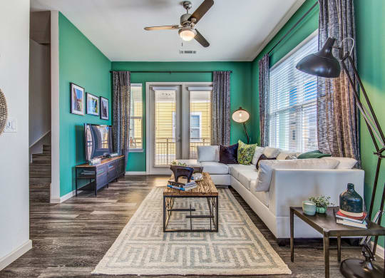 Dog Friendly Apartments in Lewisville, TX - Hebron 121 Station - Open Space Living Room with Hardwood Floors, Green Accent Walls, Ceiling Fan, Stylish Interiors, and Door that Leads to a Balcony.