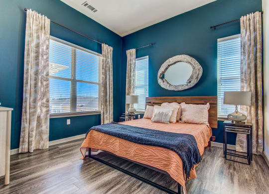 Apartments for Rent in Lewisville - Hebron 121 Station - Spacious Bedroom with Stylish Decor, Wood-Style Flooring, Large Windows, Two-Toned Walls, Bed, Nightstand, Lamps, and Dresser.