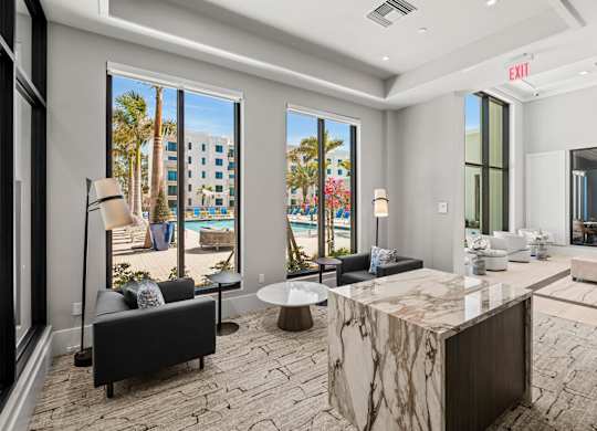 A modern living room with a marble table and a view of a pool and palm trees.
