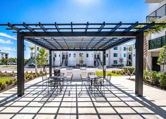 A patio with a table and chairs under a black pergola.