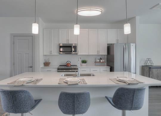 A modern kitchen with a white island and grey chairs.