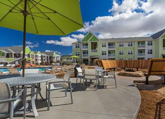 A sunny day at the poolside with a green umbrella providing shade.