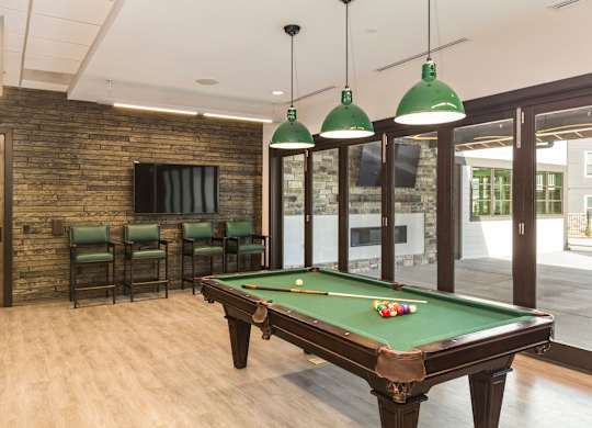 A pool table with green lampshades hanging from the ceiling.