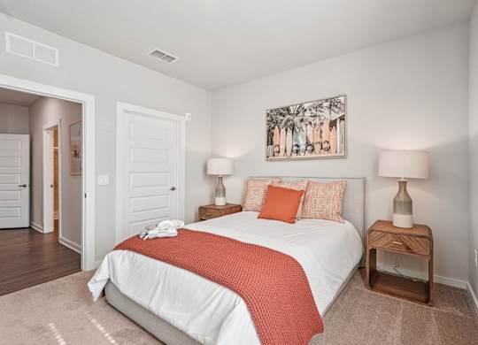 A bedroom with a bed, two lamps, and a painting on the wall.
