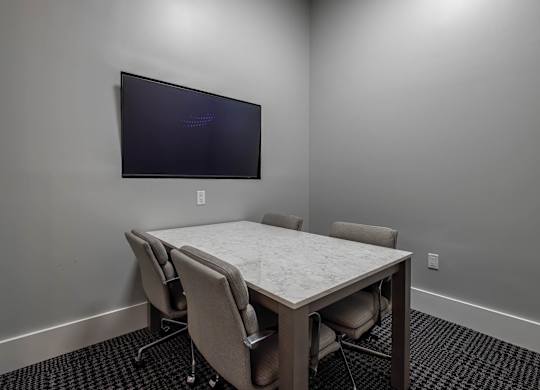 A conference room with a table, chairs, and a mounted TV screen.