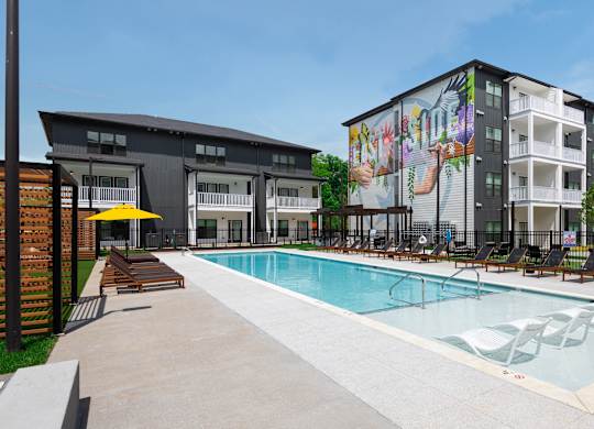 Pet-Friendly Luxury Apartments in East Nashville, TN - Flats at Laurel and Pine - Gated Resort-Style Pool with Lounge Chairs, Umbrellas, and View of Apartments Complex.