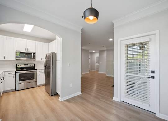 a renovated kitchen and living room with white cabinets and a door to a hallway