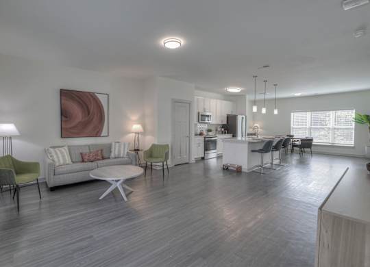 Three-Bedroom Luxury Apartments in East Nashville, TN - Flats at Laurel and Pine - Open Layout Living Room with Vinyl Plank Flooring, Couch, Armchairs, Round Coffee Table, Floor Lamp, Side Table with Lamp, and View of Kitchen.