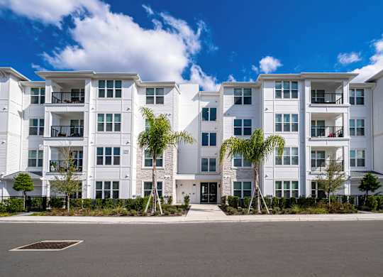 A row of white apartment buildings with balconies and trees in front.