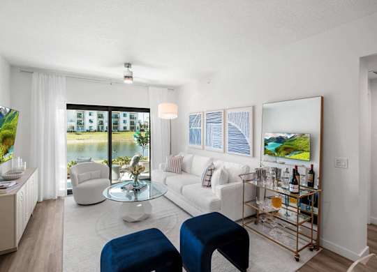 A living room with a white couch, a blue ottoman, and a glass coffee table.
