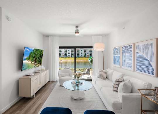 A living room with a television, a sofa, a coffee table, and a window overlooking a body of water.
