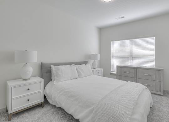 A white bedroom with a bed, nightstand, and dresser.