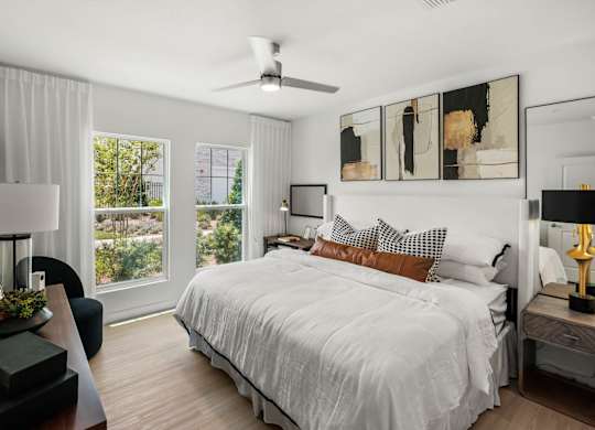 A bedroom with a large bed, a ceiling fan, and a view of trees outside the window.