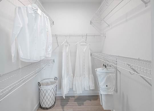 A white closet with clothes hanging and a trash can.