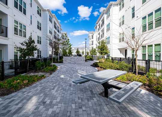 A long brick walkway leads to a white building with a black fence on the side.