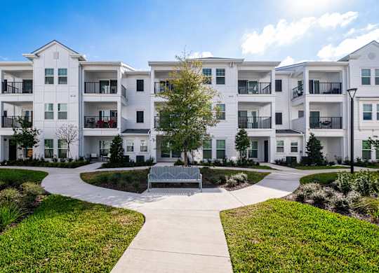 A white apartment complex with a walkway and bench in the front.