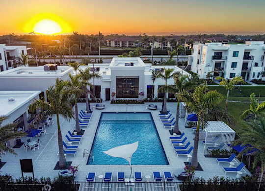 A sunset view of a pool area with lounge chairs and palm trees.