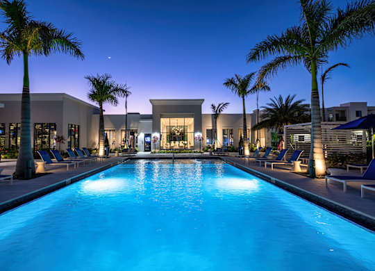 A swimming pool in front of a building with palm trees.