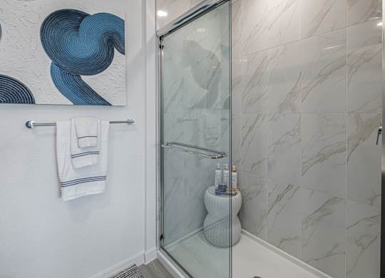 A bathroom with a glass shower door and a marble wall.
