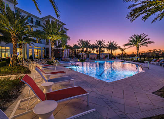 A pool surrounded by palm trees and lounge chairs.